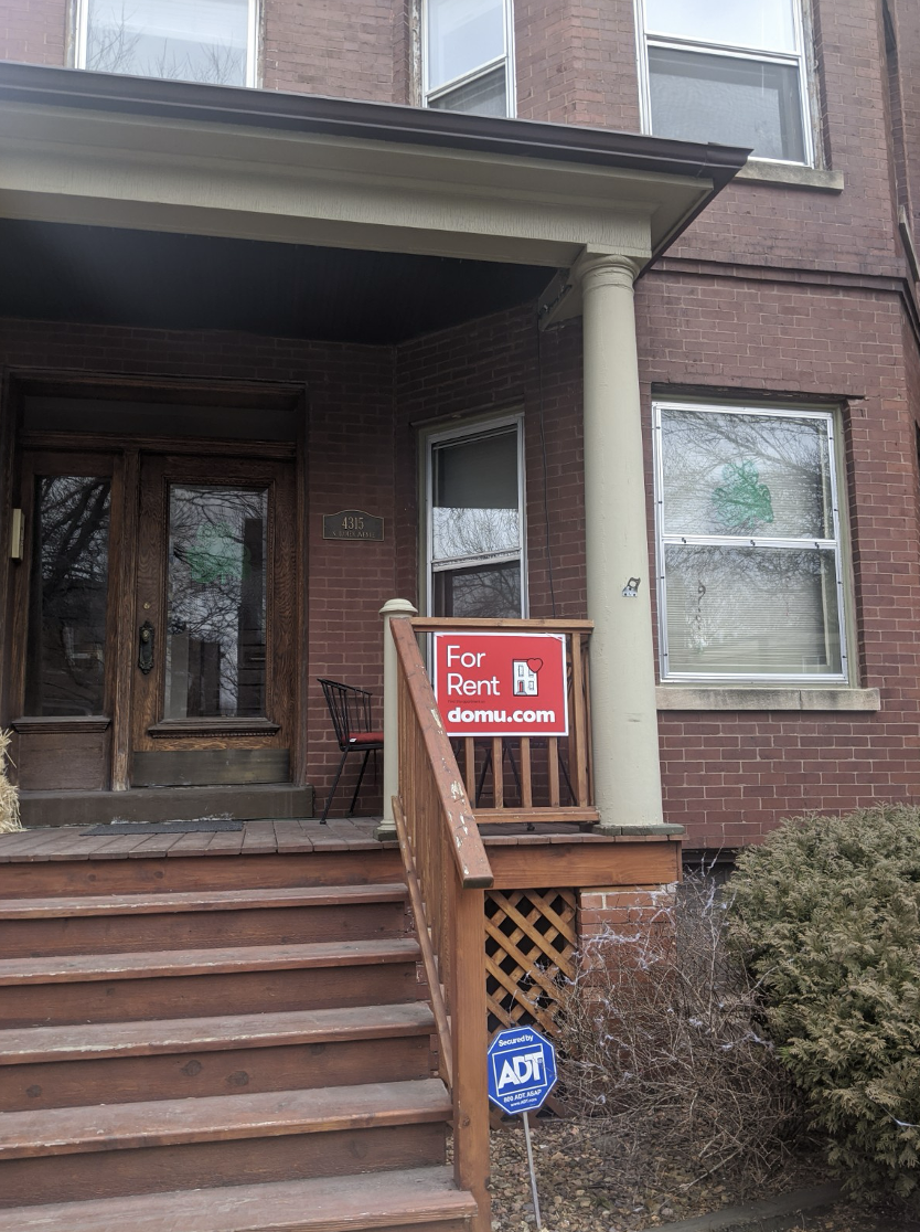 domu for rent sign displayed outside a chicago green wooden building, with a zip tie used to adhere sigange to wooden exterior fencing around the steps