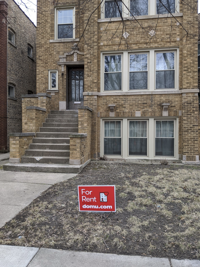 domu for rent sign installed outside a three-story brick chicago building using a lawn stake to support the sign in the soil