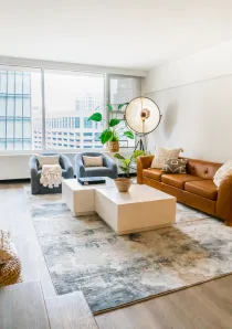 living room of Chicago apartment for rent with tan leather sofa and white coffee table in front of large windows