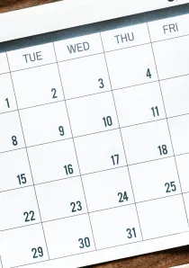 a desk calendar next to an alarm clock on a wooden desk surface