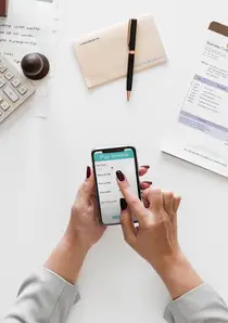 a person using a smartphone while reviewing documents on a white tabletop