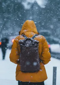 person wearing a yellow parka and black backpack and standing in a snowstorm outside of a Chicago apartment