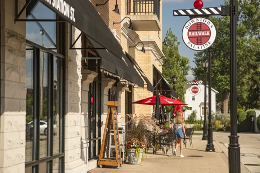 girl walkiing at railroad crossing near outdoor patio restaurant with red umbrellas in Palatine, Illinois