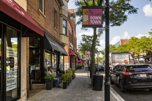 view of storefronts from sidewalk with cars parked in street on commercial street in downtown Elmhurst Illinois