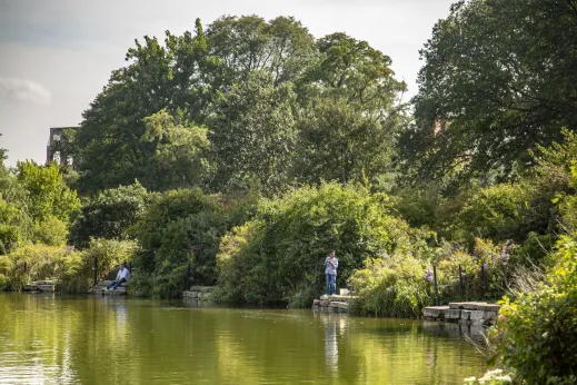 women in park fishing in pond for the edge surrounded by large beautiful trees in West Englewood Chicago