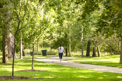 Woman walking on trail in park with lush trees all around and bright green grass in McKinley Park Chicago