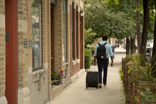 Commuter rolling suitcase on sidewalk next to brick loft storefronts in Fulton Market Chicago