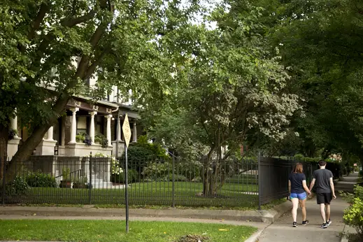 Couple holding hands and walking on sidewalk passed wrought iron fences and single family homes in Graceland West