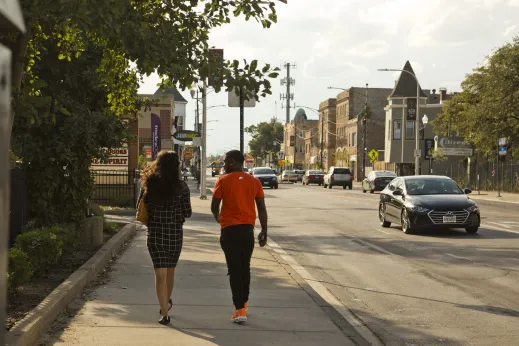 Couple walking down sidewalk by local businesses and apartments in Austin Chicago
