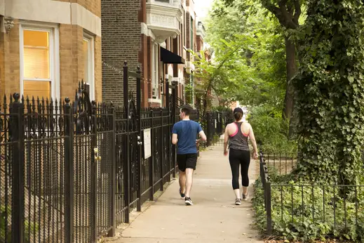 Couple walking on sidewalk passed iron fences and apartment buildings in East Village Chicago