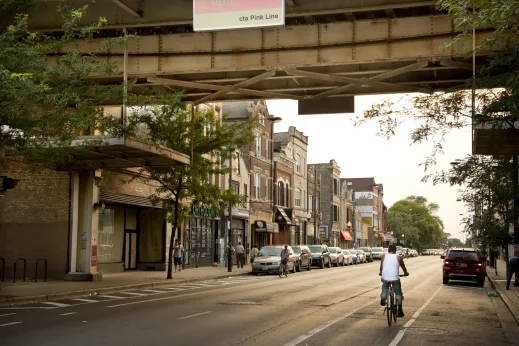 Cyclist riding in bike lane on West 18th Steet and CTA Pink line station in Pilsen