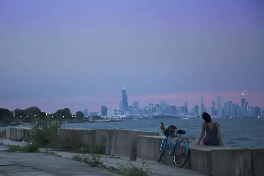 Cyclist sitting on lakefront with Chicago skyline at dusk in Hyde Park