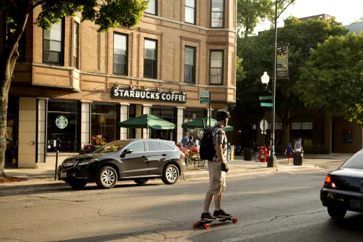 Man riding longboard across from Starbucks Coffee on W Roscoe St in Roscoe Village