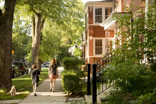 Mother and child walking dog on sidewalk by homes and apartments in St. Ben's Chicago