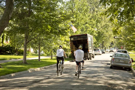 Pair of cyclists riding bikes down a residential street with a moving truck in Edison Park