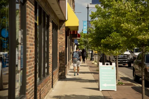 Pedestrians walking on sidewalk by local businesses on W Foster Ave in North Park Chicago