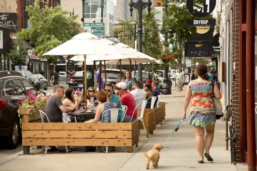 Woman walking dog down sidewalk near restaurant with patio seating in Lakeview Chicago