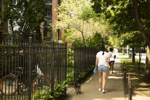 Woman walking small dog in front of wrought iron fences outside apartments in Sheridan Park