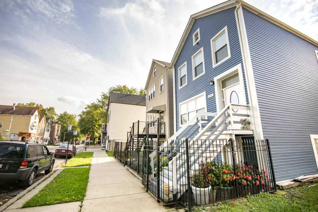 blue house with stairs up to white door along street with parked cars in Chicago Lawn