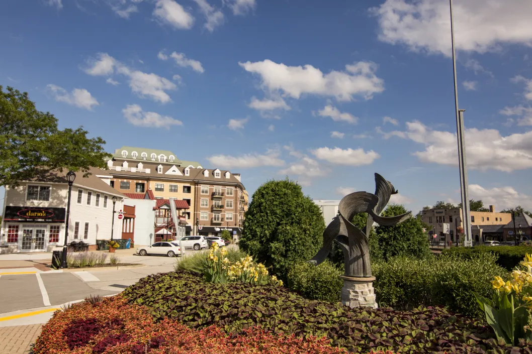 statue surrounded by flowers with brick apartment buildings in the distance in downtown Palatine, Illinois