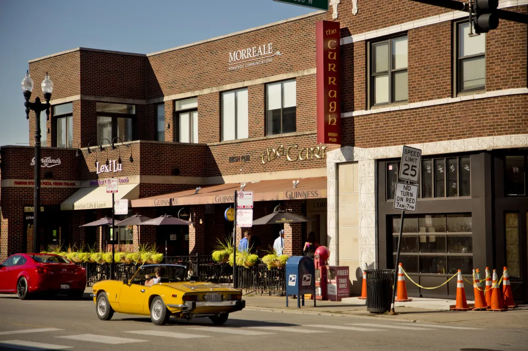 Classic convertible sports car driving in front of local businesses in Edison Park